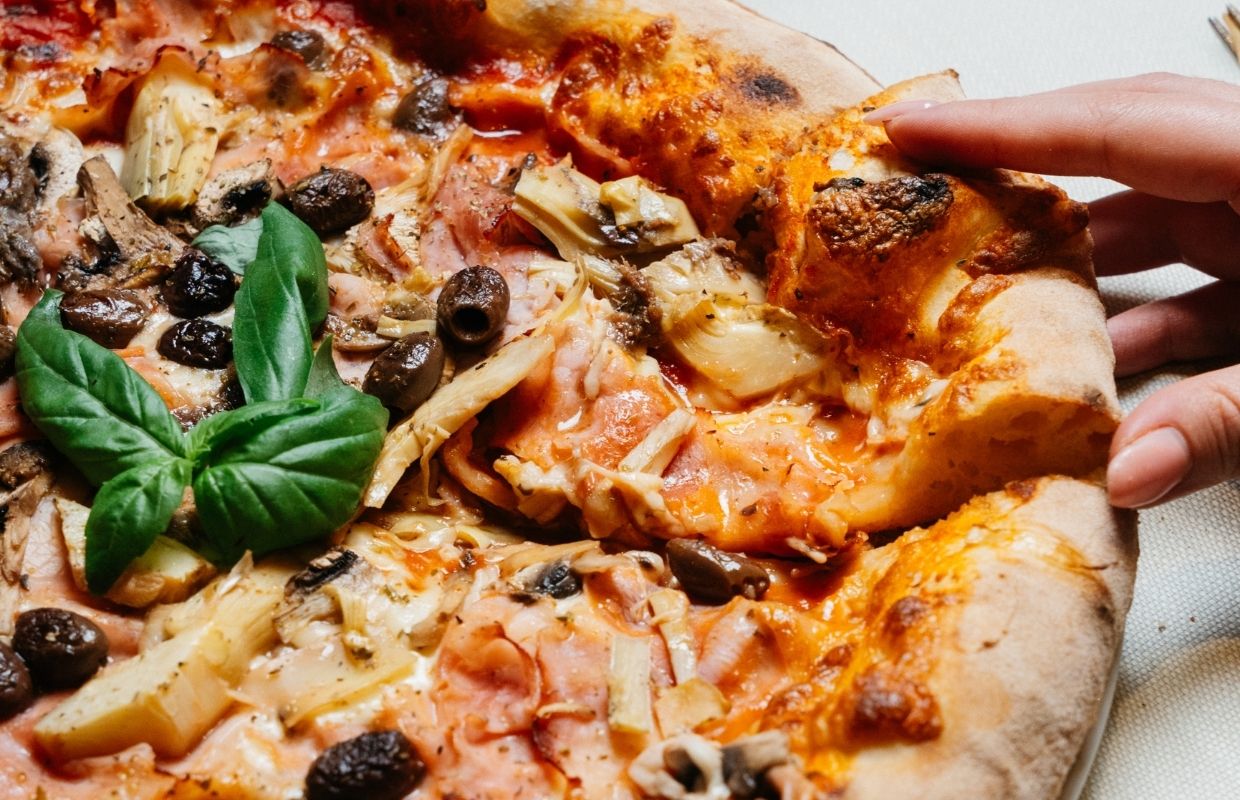 Pizza artigianale con carciofi, olive e basilico cotta nel forno a legna