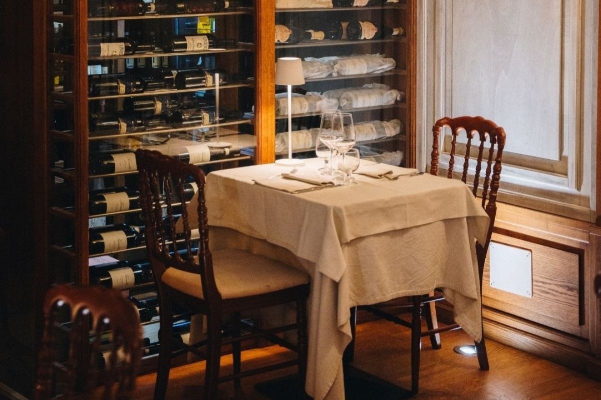 Tavolo apparecchiato con esposizione vini sullo sfondo da Il Cestino Milano